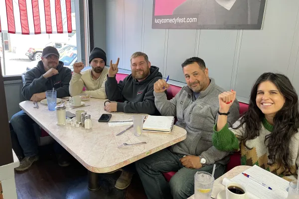 Tower Climbers and CWA organizers sit down around a diner table for breakfast, smiling at the camera with their fists raised.